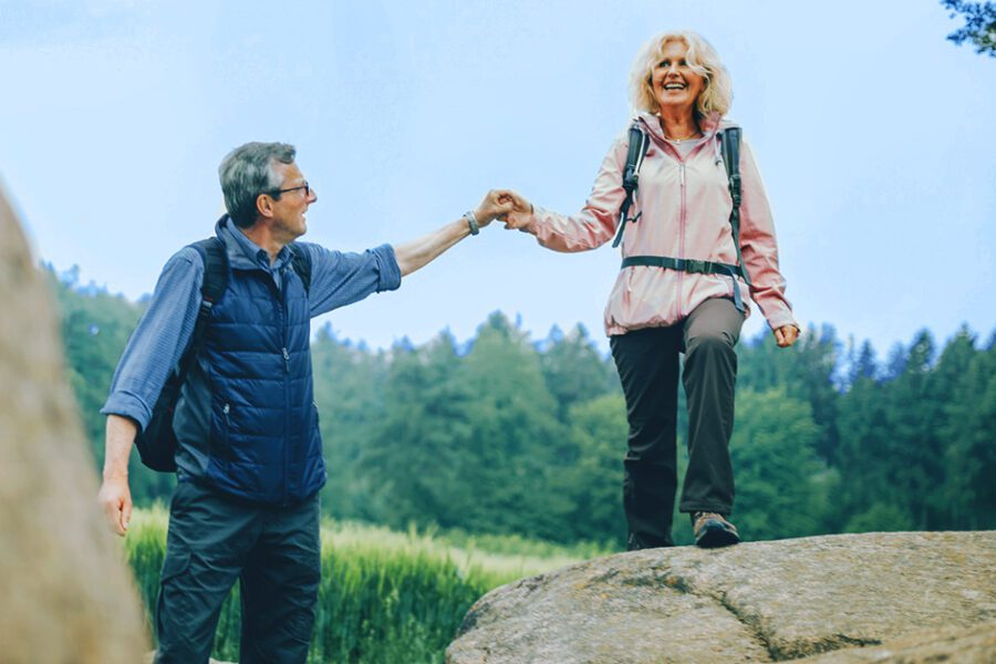 woman and man hiking. man helps woman walk along the rock. elderly couple